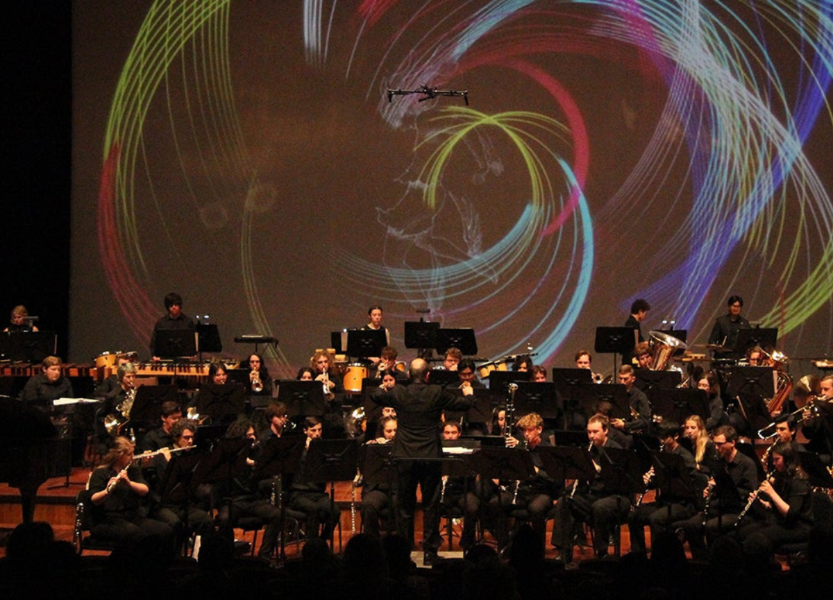 Band performs on stage with a conductor.