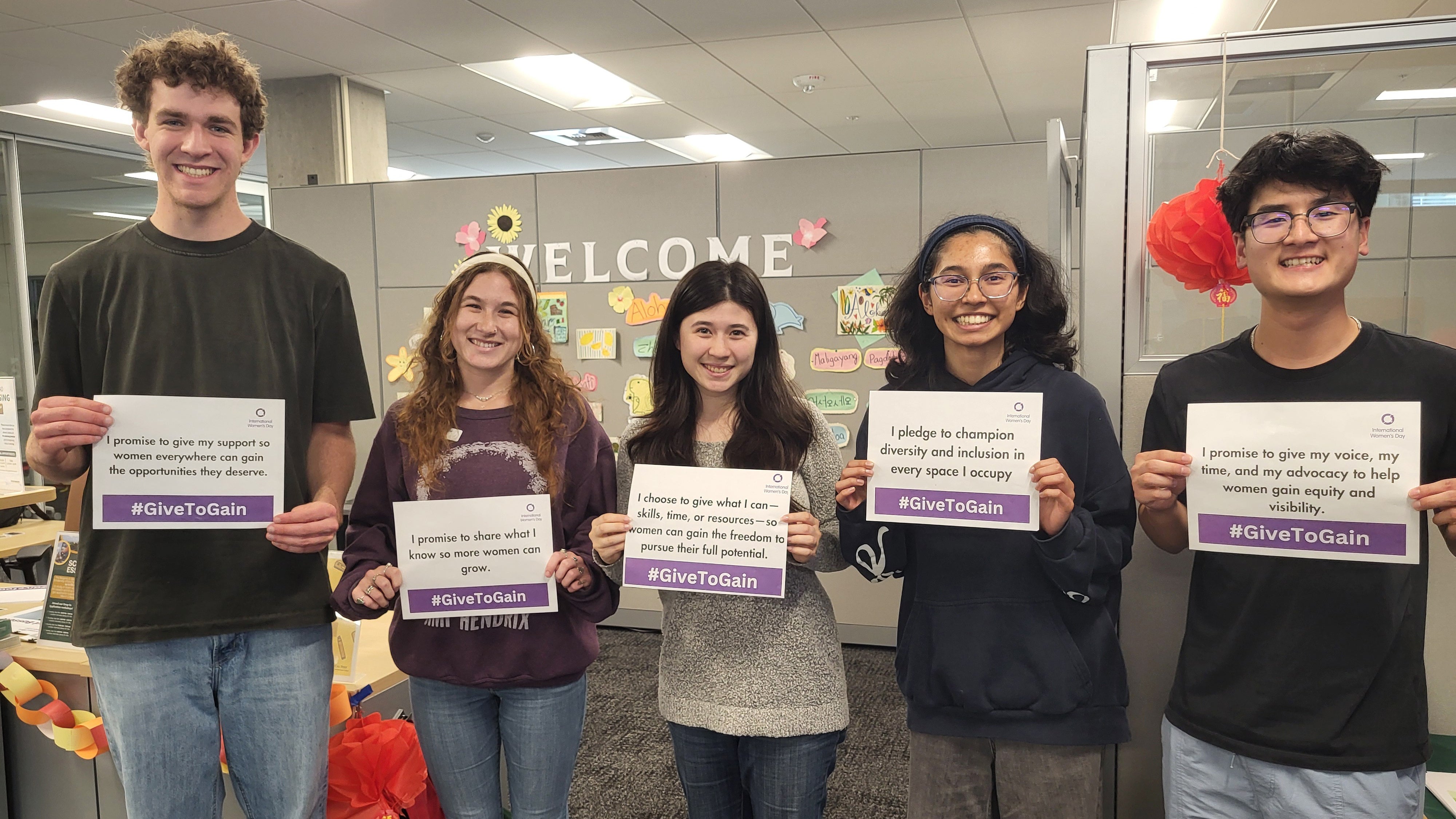 Students standing together holding signs saying how they will support women with the hashtag #GivetoGain.