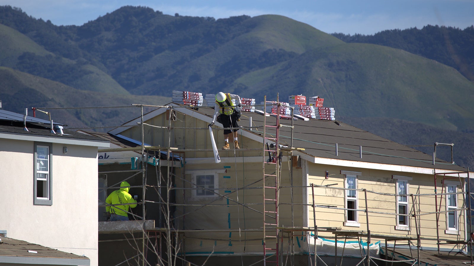 Construction workers building a house in a development with green hills in the background.