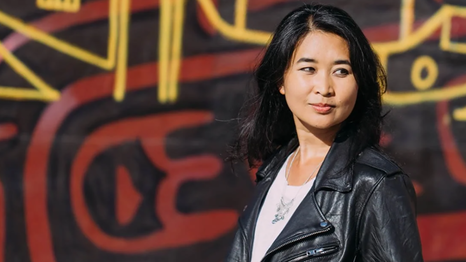 Artist and writer Thi Bui standing in front of a painted wall.