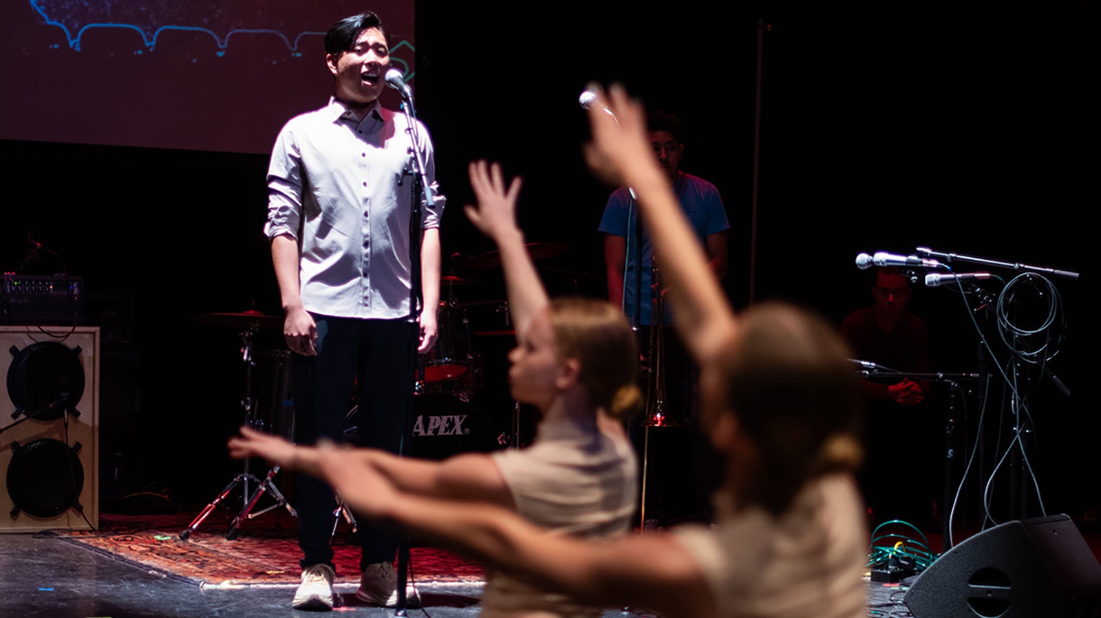A Cal Poly Soundings singer on stage performing with dancers dancing in the foreground.