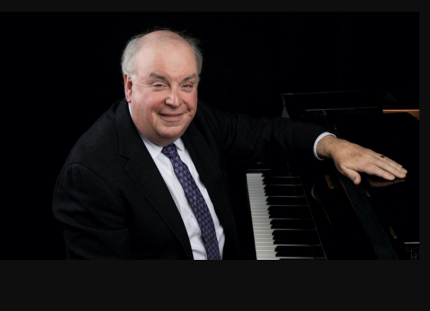 Dr. Terrence Spiller sits at the piano in a dark suit and tie
