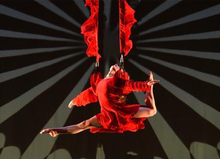 Woman in red dress, suspended from trapeze. 