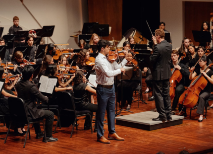 Violinist plays on stage with symphony in background.