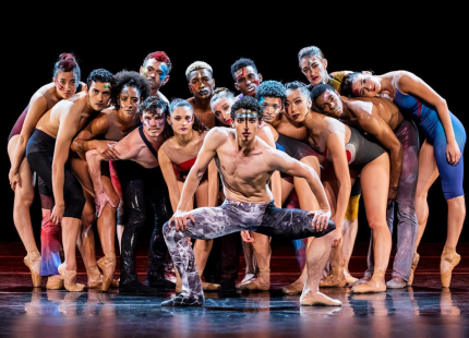 Dancers pose on stage as a group.