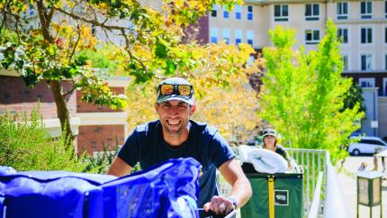 Smiling person pushing a green moving bin of belongings near campus apartments