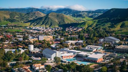 An aerial view of the Cal Poly campus with green hills and a blue sky.