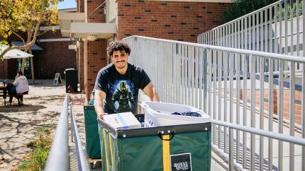 A student pushing a big cart of personal belongings up a ramp into a dorm.