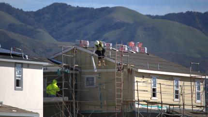 Construction workers building a house in a development with green hills in the background.