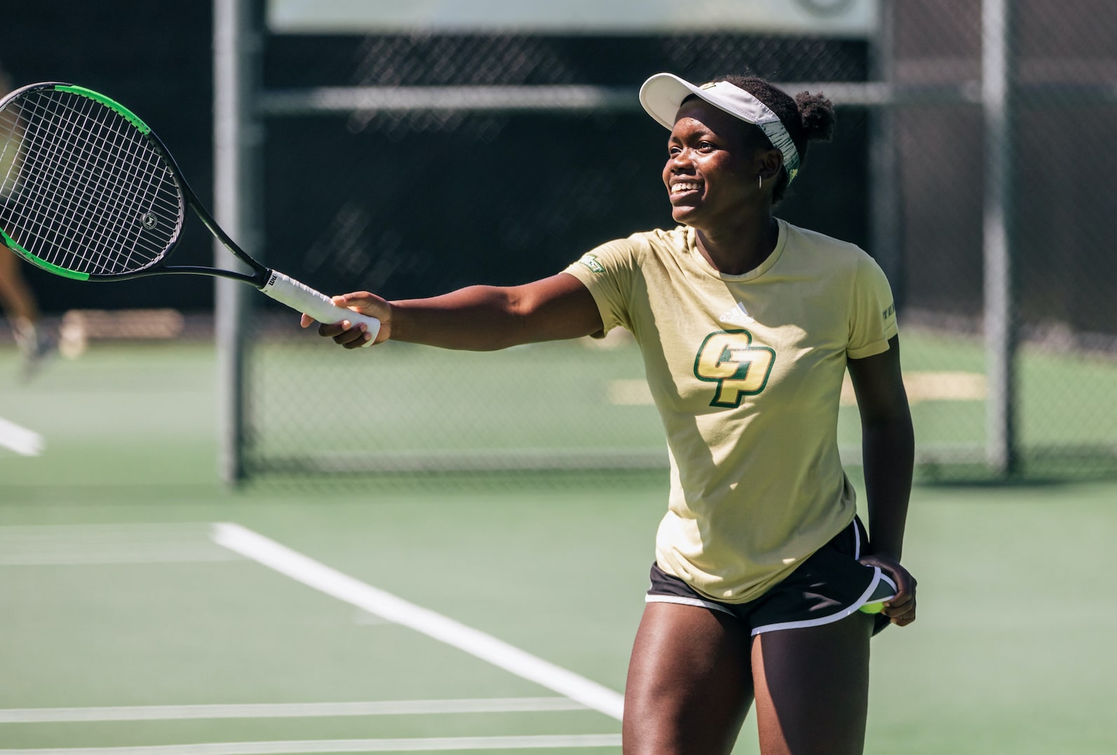 Member of Cal Poly women's tennis team in yellow shirt and green shorts on the court
