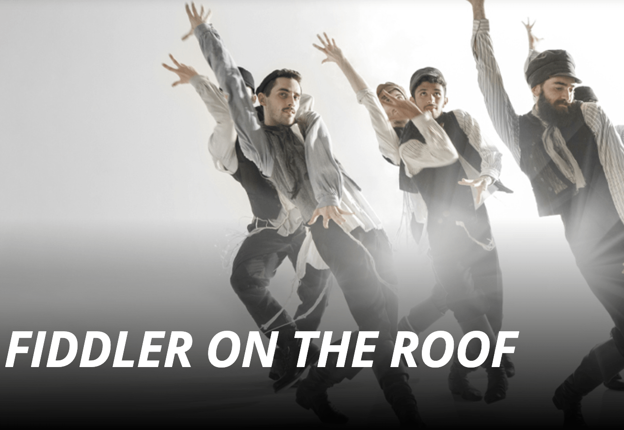 Photo of dancers from cast of Fiddler on the Roof in full costume. The words Fiddler on the Roof appear in white along the bottom of the photo. 