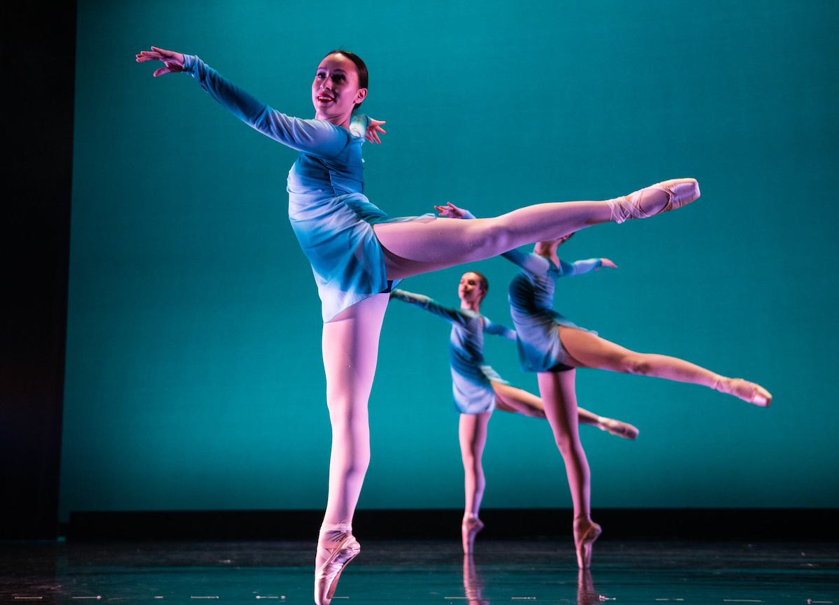 Three dancers dressed in blue are poised on pointe on the Spanos stage