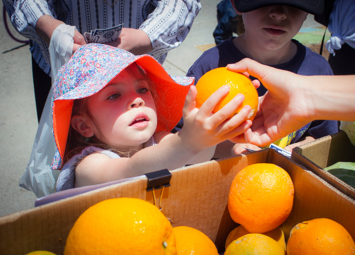 Small child gets orange from SLO Food Bank volunteer