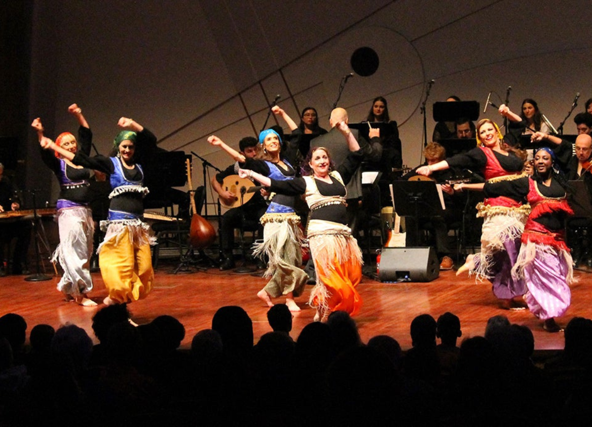 Dancers dance on stage dressed in Arab attire.